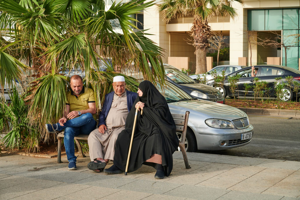 Beirut, Lebanon - April 30, 2019: two lebanese man and a woman enjoy a moment of relax on a bench along General De Gaulle road.